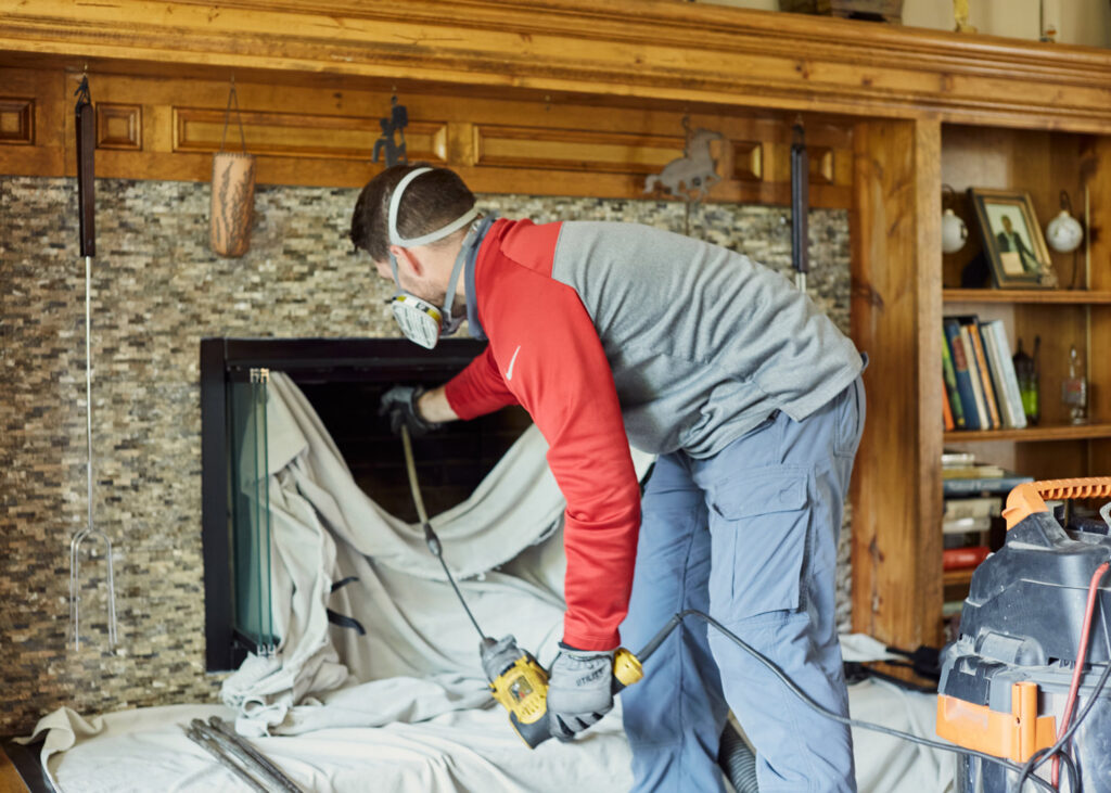 A chimney sweep technician working inside a home, wearing a mask, for Full Service Chimney in Overland Park, KS