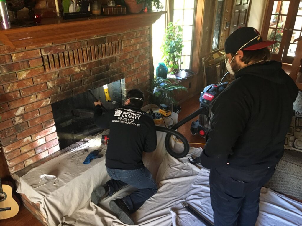 Two chimney sweep technicians cleaning a fireplace with a vacuum hose for Northwest Chimney in Bremerton, WA.