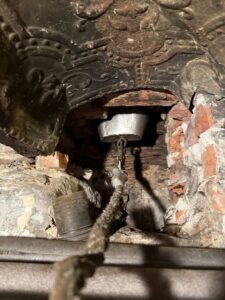 A chimney sweep tool with a rope and bucket-like attachment inside a flue by Certified Masons in Warwick, RI