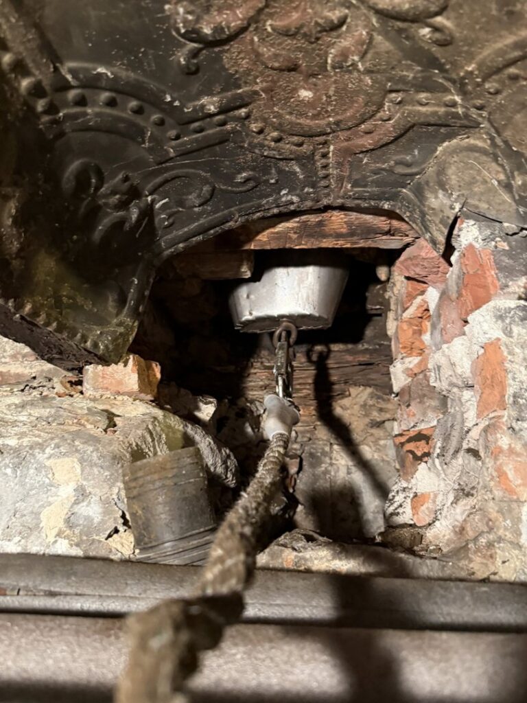 A chimney sweep tool with a rope and bucket-like attachment inside a flue by Certified Masons in Warwick, RI