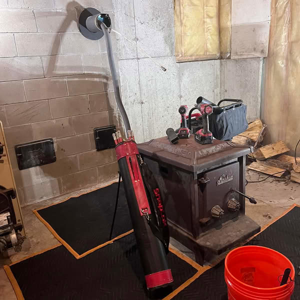 Chimney sweep tools and equipment set up next to a wood stove in a basement for a job by Granite State Chimney in Manchester, NH