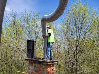 A chimney sweep worker on a roof using a large hose for cleaning at Midwest Chimney Repair in Maple Lake, MN.