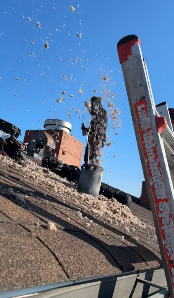 Soot and debris being swept from a chimney on a Brooklyn rooftop by Chimney Sweep Service LLC.
