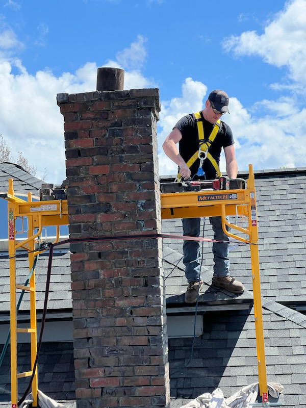 A chimney technician on scaffolding servicing a brick chimney for Western Expanse Chimney and Hearth in De Smet, ID.