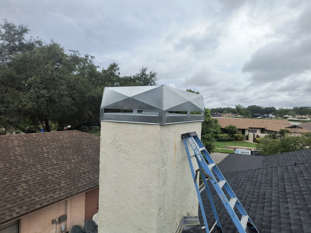 A chimney with a newly installed metal cap and a ladder leaning against it, indicating work by A Sweep Across the Bay in Parrish, FL.