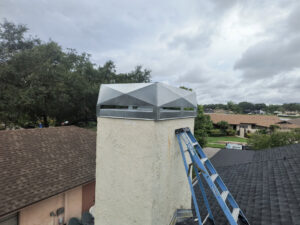 A chimney with a newly installed metal cap and a ladder leaning against it, indicating work by A Sweep Across the Bay in Parrish, FL.