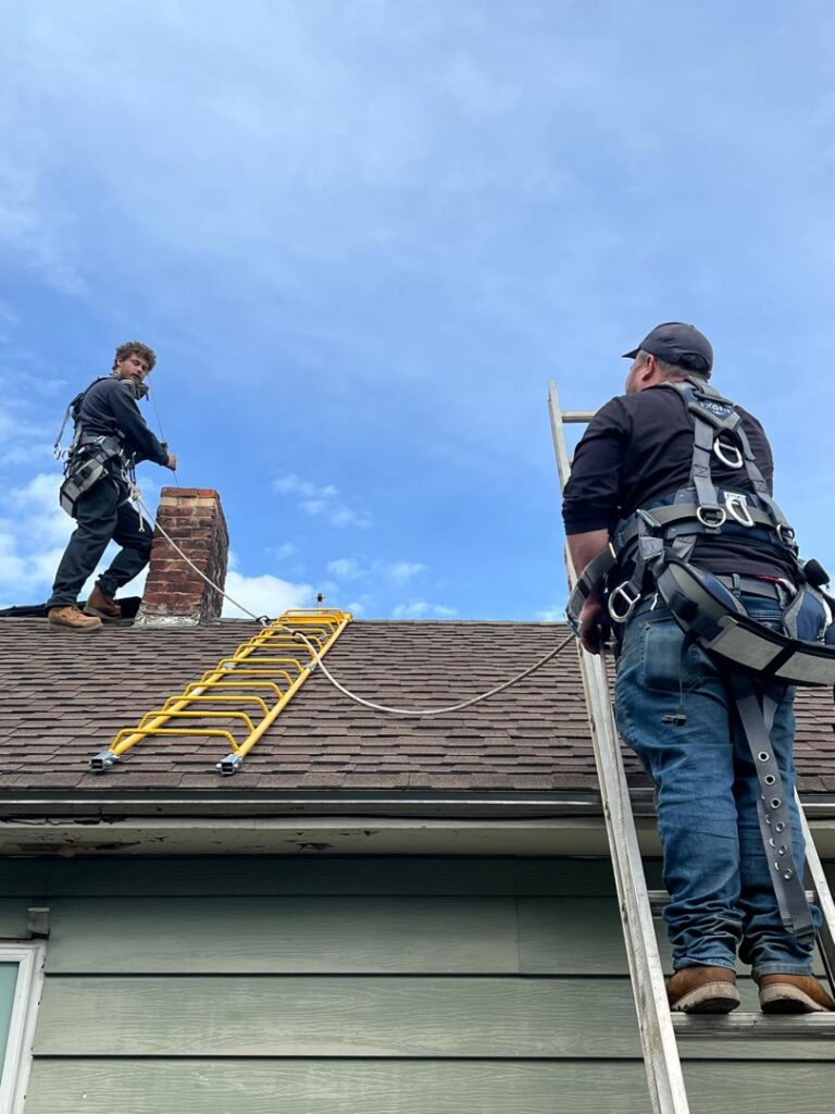 Two Chimney Wizards LLC technicians on a roof with ladders and safety gear, preparing for chimney service in Orofino, ID.
