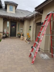 A ladder with GET LIT Electrical branding and boxes of Christmas lights for installation in Glendale, AZ.