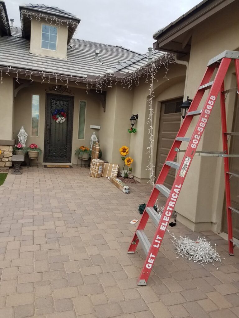 A ladder with GET LIT Electrical branding and boxes of Christmas lights for installation in Glendale, AZ.