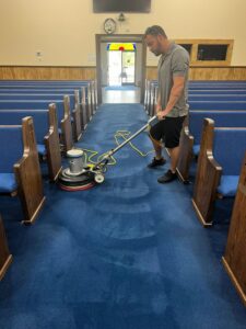 A technician performing professional carpet cleaning in a church aisle with blue carpet by All Ways Organic Citrus Carpet & Upholstery Cleaning in Wilmington, NC.