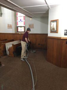 A professional from Yellow Finch Carpet Cleaning LLC cleaning brown carpet in a church, providing commercial services in Dover, NH.