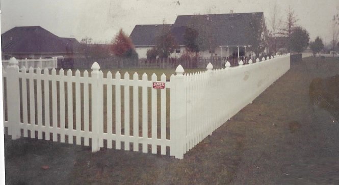 A classic white picket fence with decorative post caps and a James Fencing LLC sign, installed in Columbia, MO.