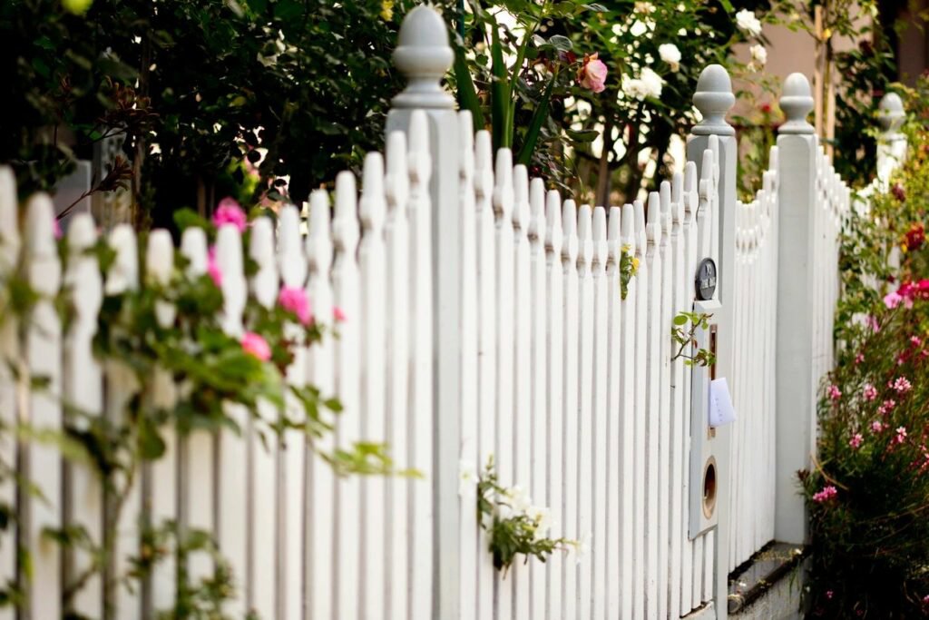 A beautiful classic white picket fence adorned with flowers, maintained by Walt's Fence Staining in Allen, TX.