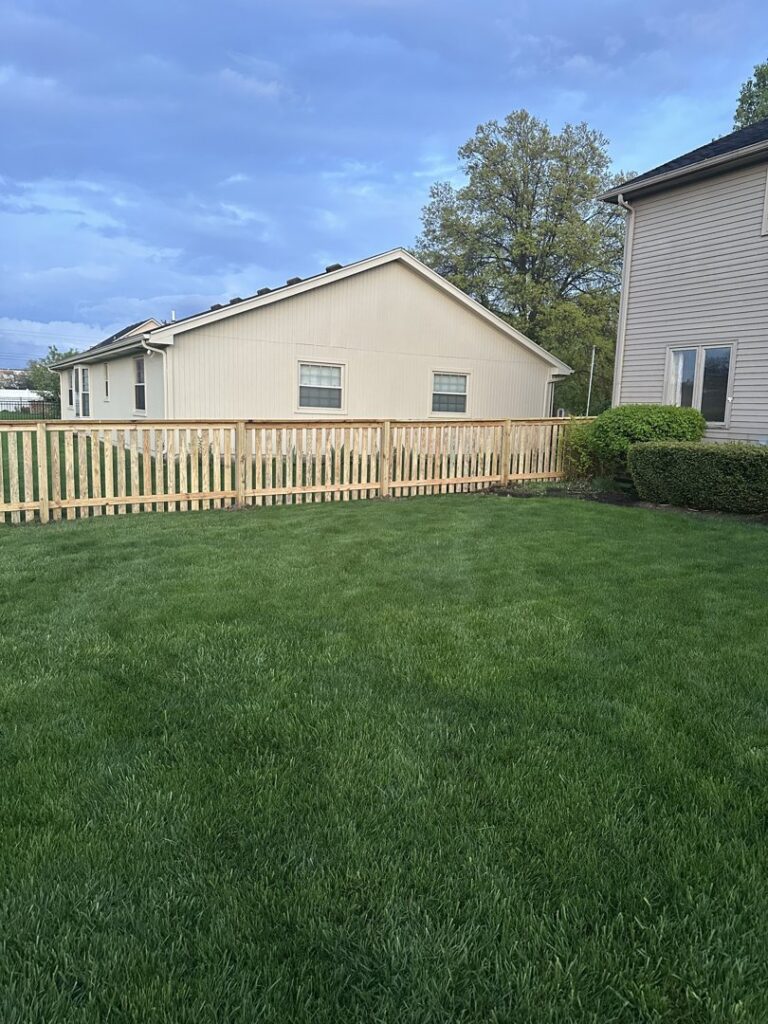 A classic wooden picket fence installed around a lush green backyard by NBBJ Fence LLC in Bluffton, IN.