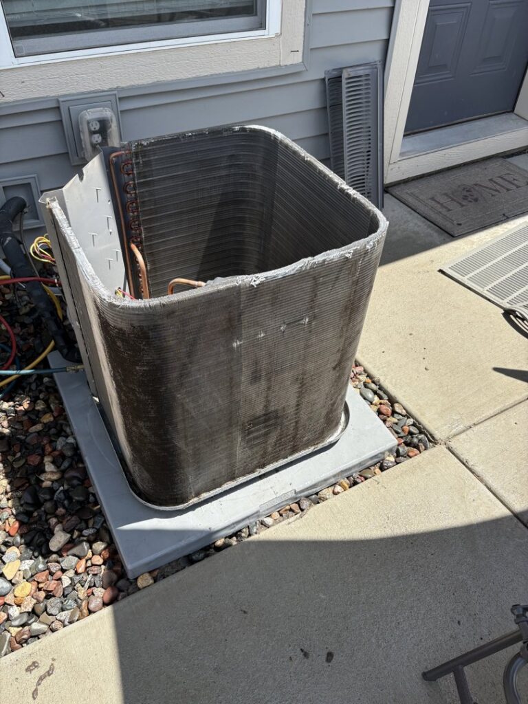 Clean coils of an outdoor air conditioning unit with the side panel removed, indicating recent service or inspection by Holzer Heating And Cooling in Savage, MN