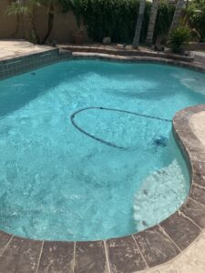 A sparkling clean blue pool with a pool cleaning hose visible, indicating ongoing maintenance by Prime Pool Care in Satellite Beach, FL.