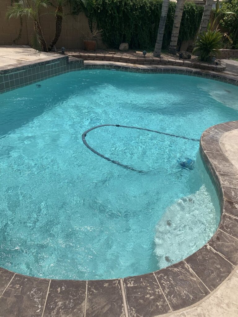 A sparkling clean blue pool with a pool cleaning hose visible, indicating ongoing maintenance by Prime Pool Care in Satellite Beach, FL.