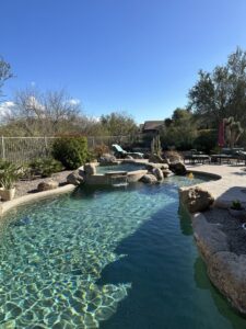 A sparkling clean pool with a rock waterfall and a pool vacuum hose, maintained by Pool Scouts of Scottsdale in Scottsdale, AZ.
