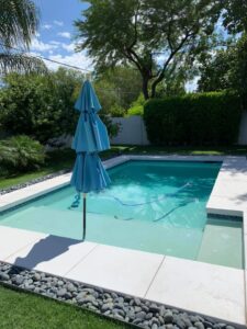 A beautifully clean pool with a blue umbrella, showcasing the results of professional pool cleaning by Space Ranger Pools in Gilbert, AZ.