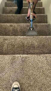 A professional cleaning technician from Raysco, Inc. cleaning carpeted stairs with a specialized wand in Las Vegas, NV.