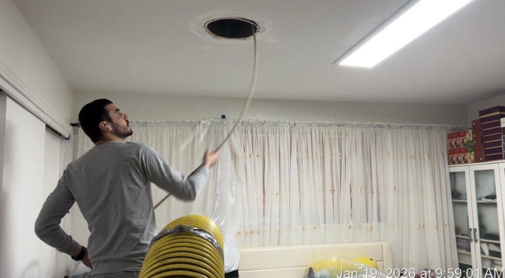 A technician using specialized tools to clean a ceiling air duct opening, ensuring fresh air for Duct Doctor of Baton Rouge, LA clients.