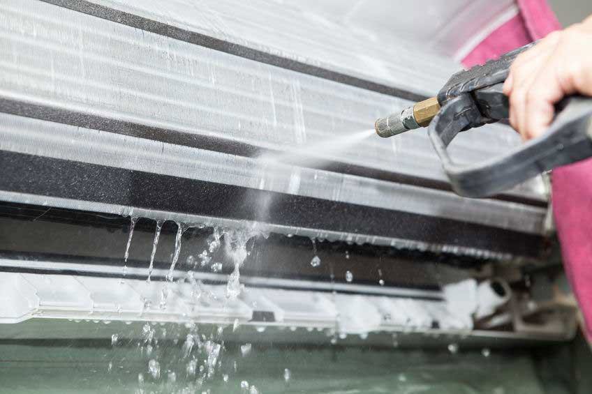 A technician cleaning the coils of an indoor air conditioning unit with a pressure washer for Premier Comfort Service Company in San Antonio, TX.