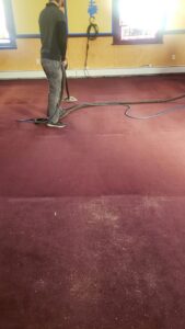 A professional technician cleaning a large red carpet with a wand, showing areas before and after cleaning, by Fantastic Carpet Cleaning NYC in Ridgewood, NY