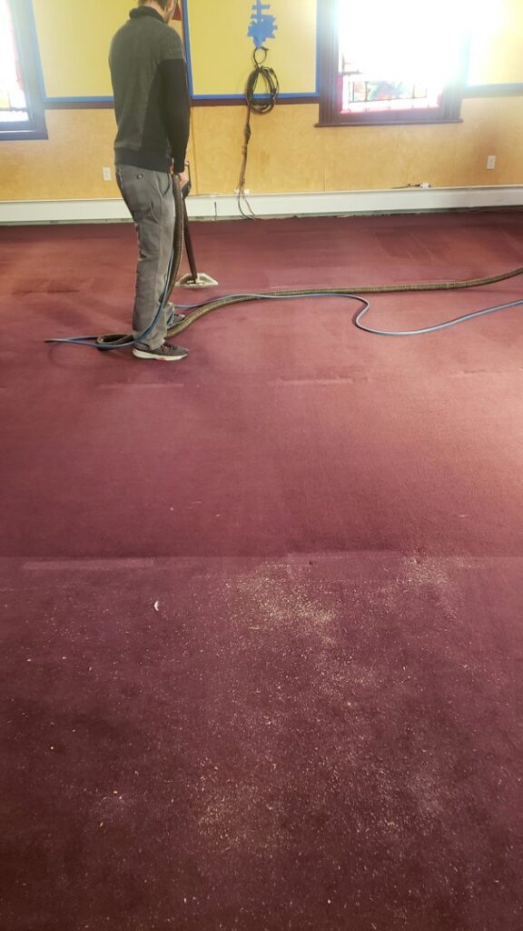 A professional technician cleaning a large red carpet with a wand, showing areas before and after cleaning, by Fantastic Carpet Cleaning NYC in Ridgewood, NY