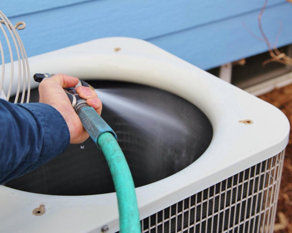 A technician cleaning an outdoor air conditioning condenser unit with a hose for Meyer's Air Conditioning & Refrigeration Co in Phoenix, AZ.