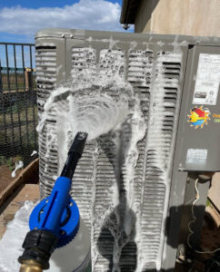 A technician cleaning an outdoor HVAC condenser unit with foam as part of routine maintenance by Blue Collar Mechanical LLC in Indianapolis, IN.