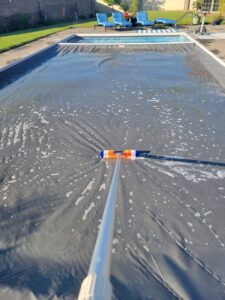 A person using a brush to clean a pool cover, part of comprehensive pool maintenance by Westside Pools in Owensboro, KY.