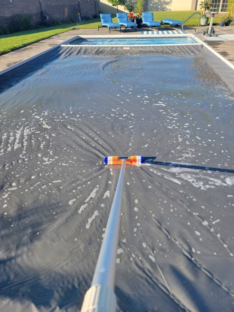 A person using a brush to clean a pool cover, part of comprehensive pool maintenance by Westside Pools in Owensboro, KY.