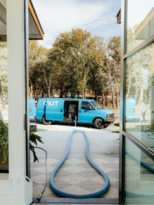 A Coconut Cleaning of Dallas-Fort Worth van with hoses extended into a home for a professional cleaning service in Dallas, TX.