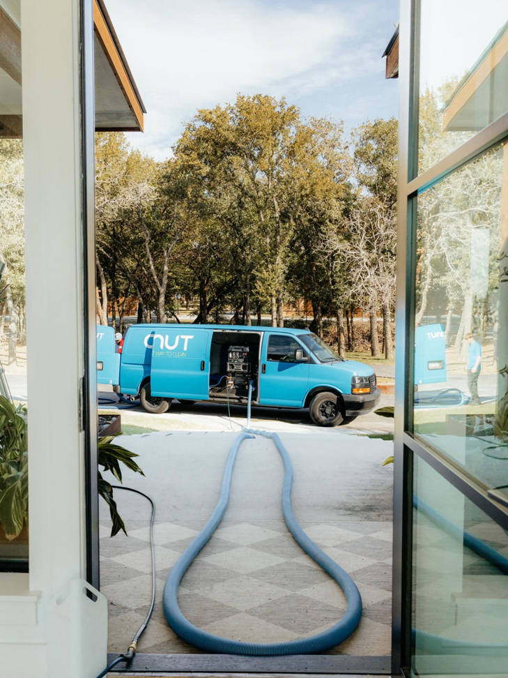 A Coconut Cleaning of Dallas-Fort Worth van with hoses extended into a home for a professional cleaning service in Dallas, TX.