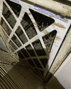A severely clogged HVAC air filter visible in a return vent, serviced by B & H Heating and Air Services LLC in Local City, ST.