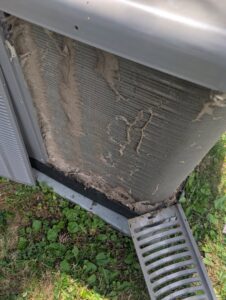 Heavily clogged exterior coils of an outdoor AC unit, indicating a need for cleaning by Falso Service Experts in East Syracuse, NY.