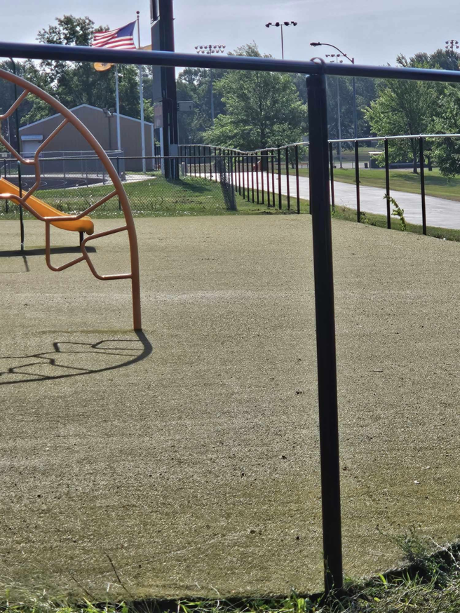 A close-up view of a black chain-link fence post and fence line near a playground, installed by Atchison Fence in Effingham, KS.