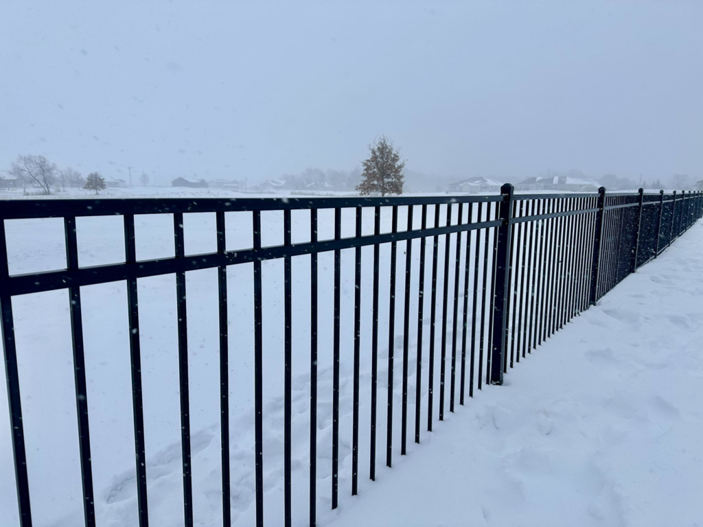 A close-up view of a black ornamental fence post and rails against a snowy background by JD Fencing LLC in Boone, IA.