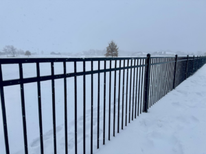 A close-up view of a black ornamental fence post and rails against a snowy background by JD Fencing LLC in Boone, IA.