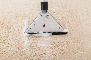 A close-up view of a carpet cleaning wand with cleaning foam on a beige carpet by Steamway Carpet Cleaning in El Paso, TX