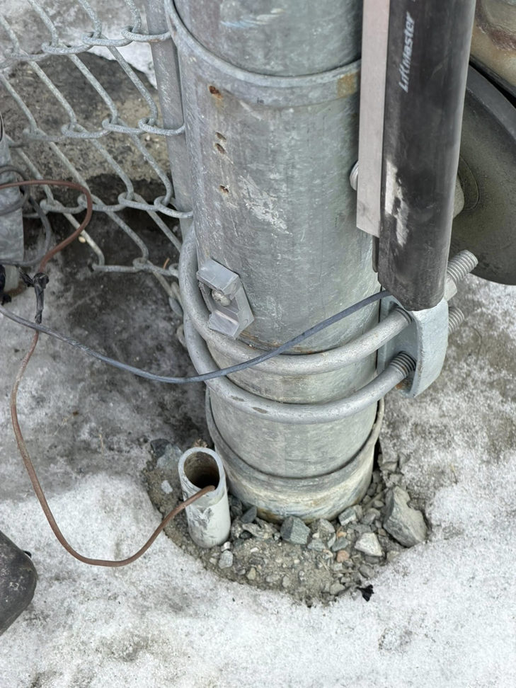 A close-up view of a chain-link fence post installation with wiring and hardware by Wayside Fences in Brattleboro, VT.