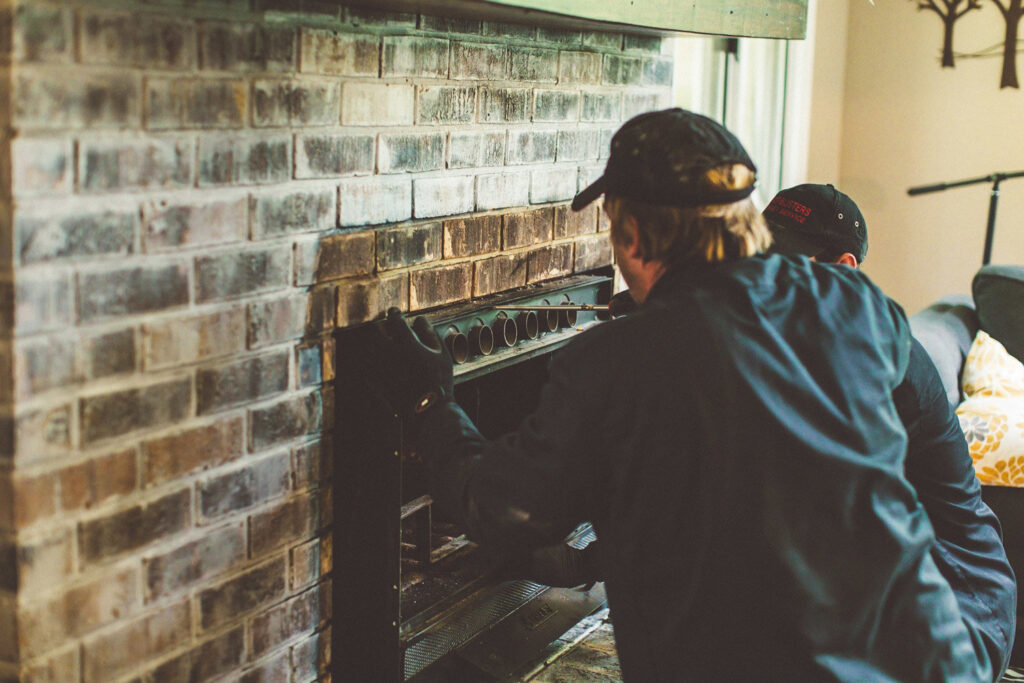 A close-up of two chimney sweeps from Soot Busters working on a fireplace insert during a service call in Birmingham, AL.
