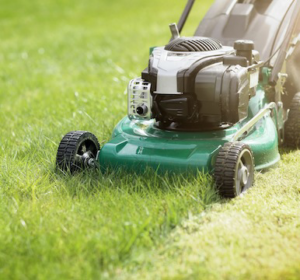 A close-up view of a green lawnmower actively cutting lush green grass for Green Arbor Landscaping in Renton, WA.