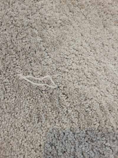 A close-up view of light-colored carpet with a loose thread, showcasing carpet quality by Advanced Flooring in Appleton, WI.