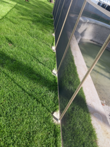 A close-up view of a light-colored mesh pool fence installation by All Brand Pool Fence in Fort Lauderdale, FL.