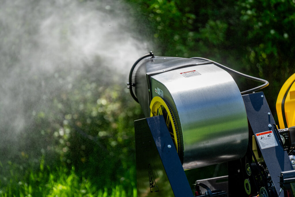 A close-up of a mosquito sprayer attachment actively dispersing treatment in a green landscape for Fog'em Mosquito Control in Bismarck, ND.