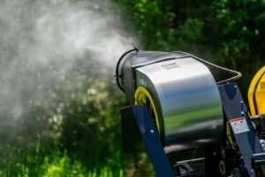 A close-up of a mosquito sprayer attachment actively dispersing treatment in a green landscape for Fog'em Mosquito Control in Bismarck, ND.
