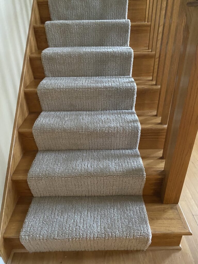 A close-up view of a newly installed grey carpet runner on wooden stairs by At Home Flooring in Naperville, IL.