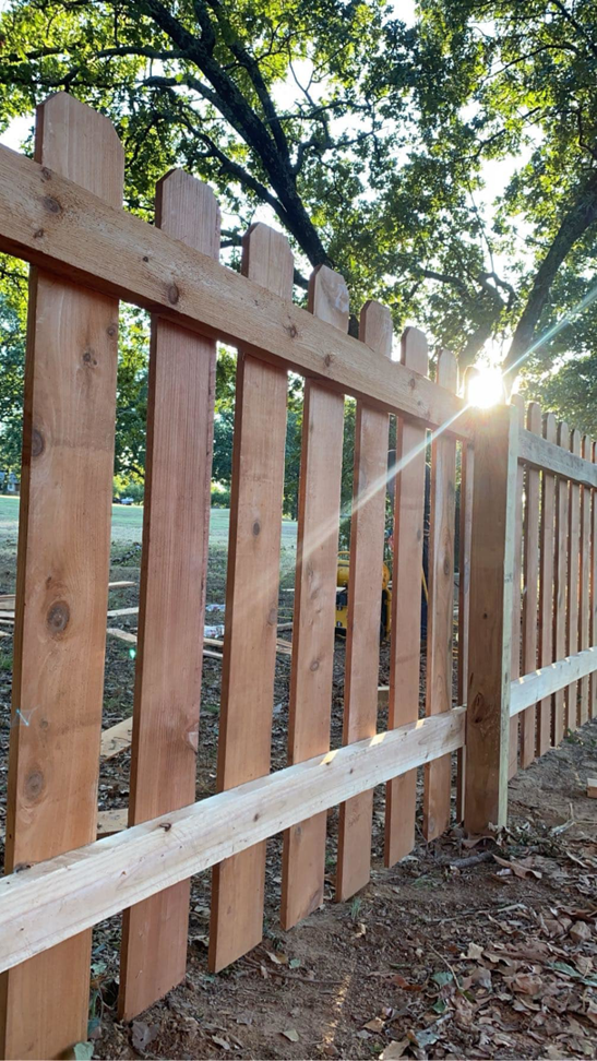 A close-up view of a new wooden picket fence installed by Fianna Fencing Company in Fort Smith, AR, with sunlight.