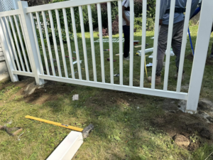 A close-up view of a newly installed white fence post set in the ground by T & A Fencing in Warren, MI, with tools nearby.